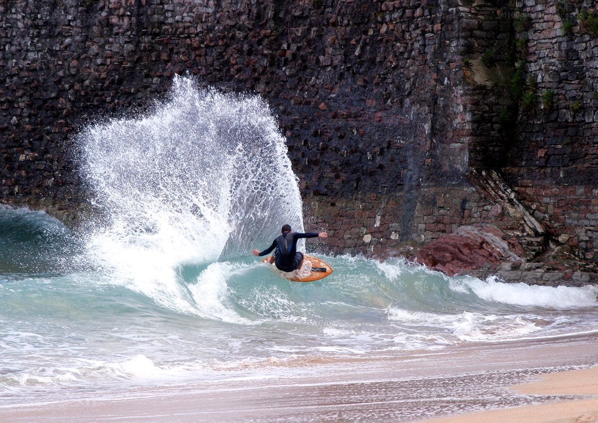 Surfer riding wave near cliff