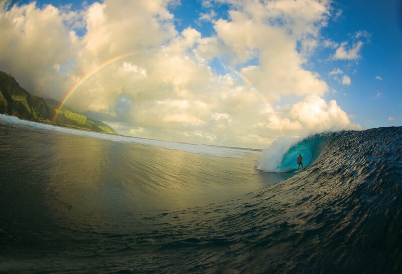 Surfer riding wave under rainbow
