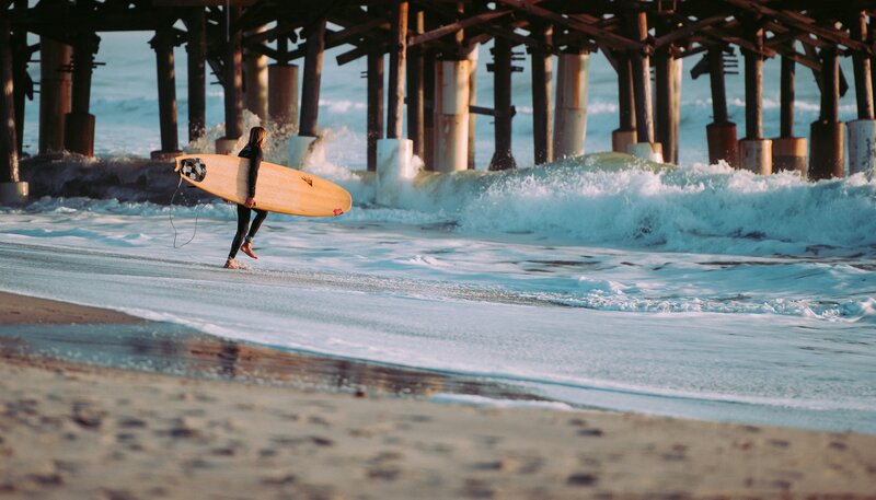 Surfer walking under pier