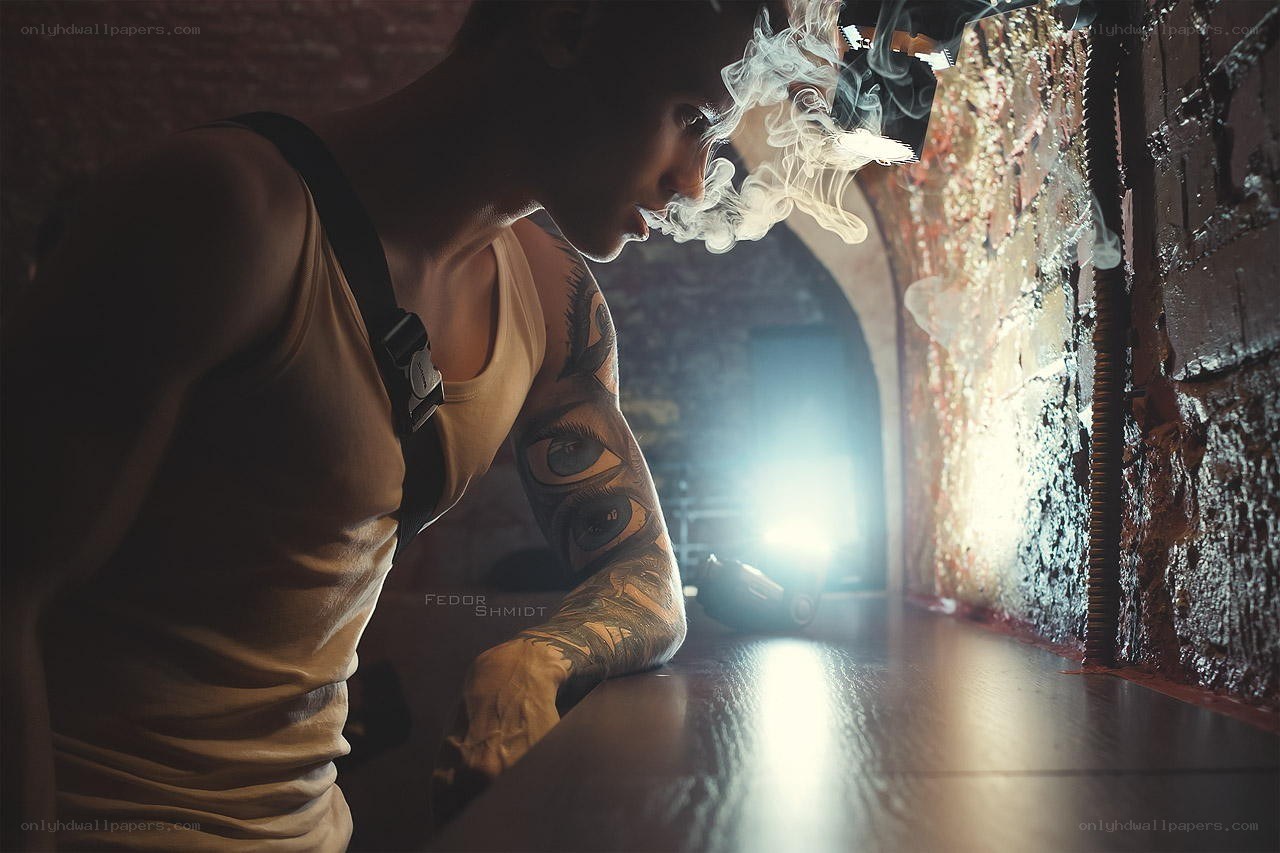 tattooed man smoking in dim room