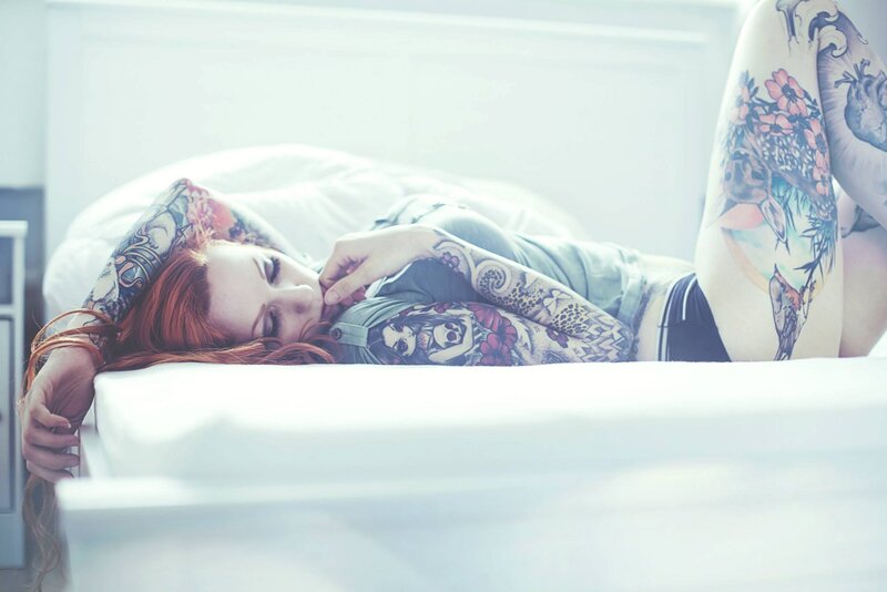 tattooed woman resting on bed