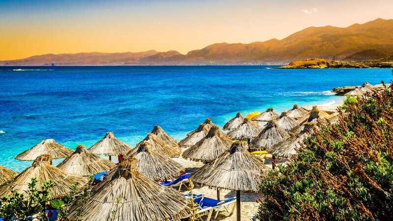 Thatched Umbrellas on Beach — Blue, Serene, Sunset, Photograph, Sea, Mountains
