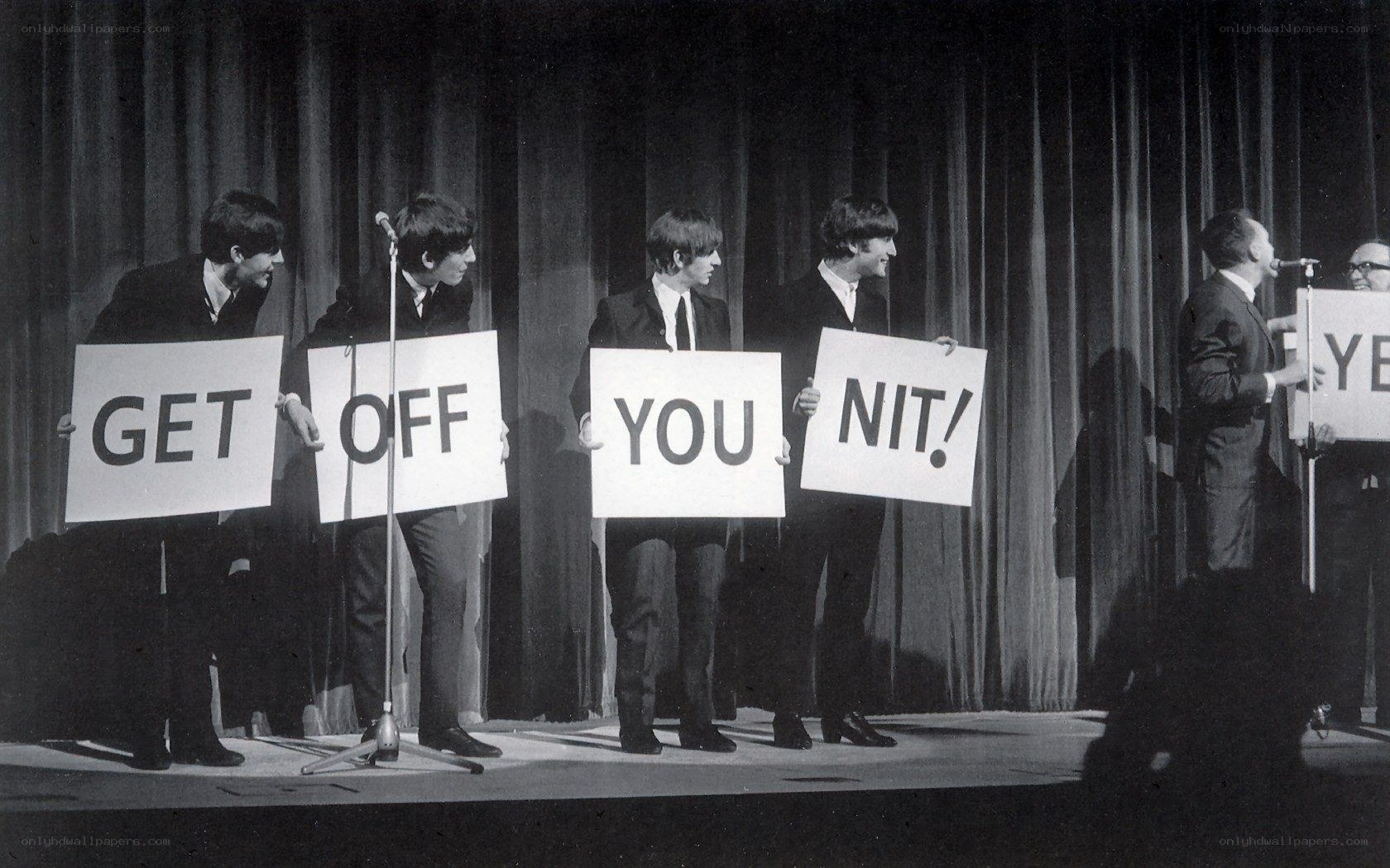 The Beatles hold signs on stage