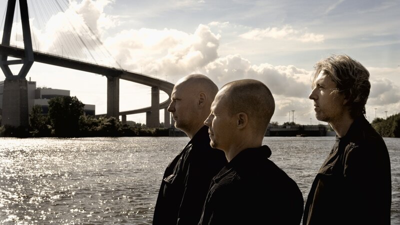 Three men by a river with a bridge