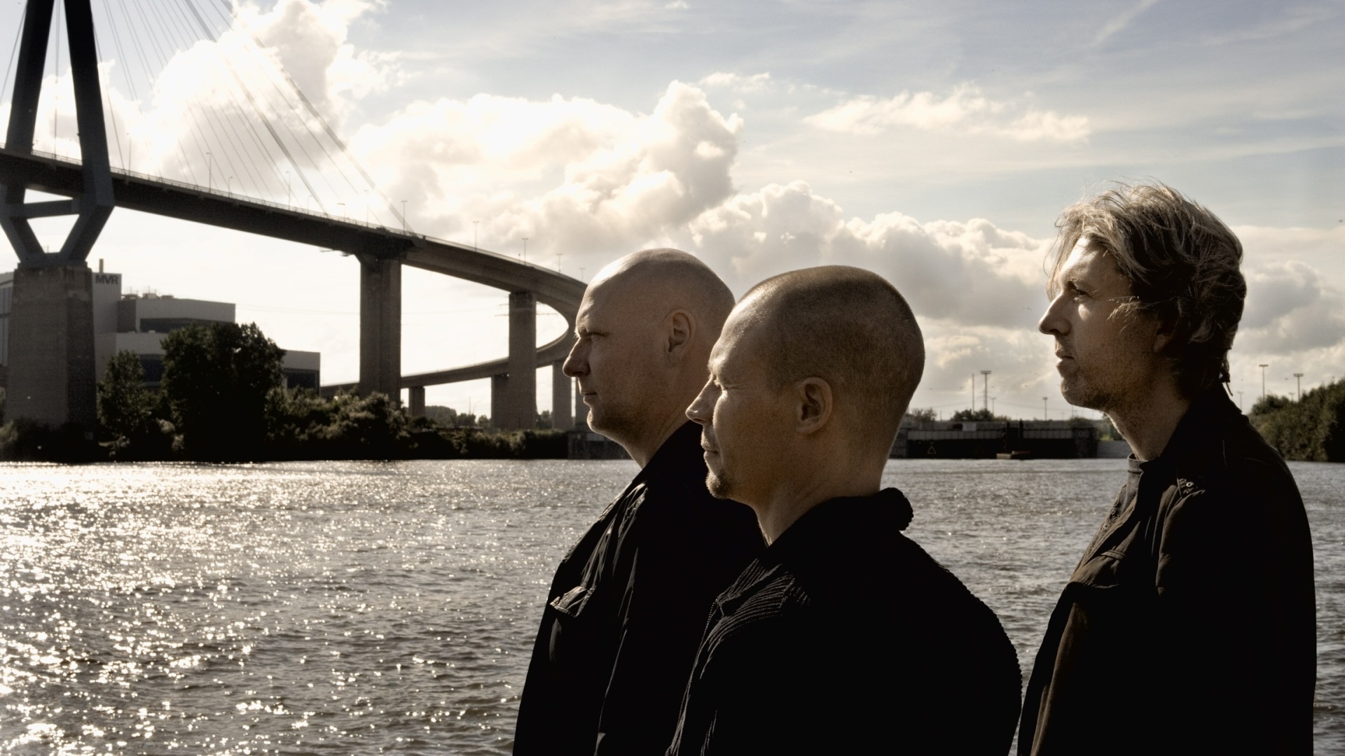 Three men by a river with a bridge