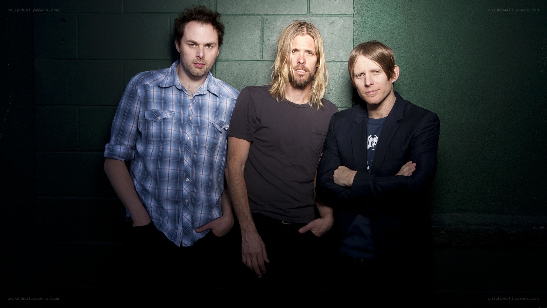three men posing against a wall