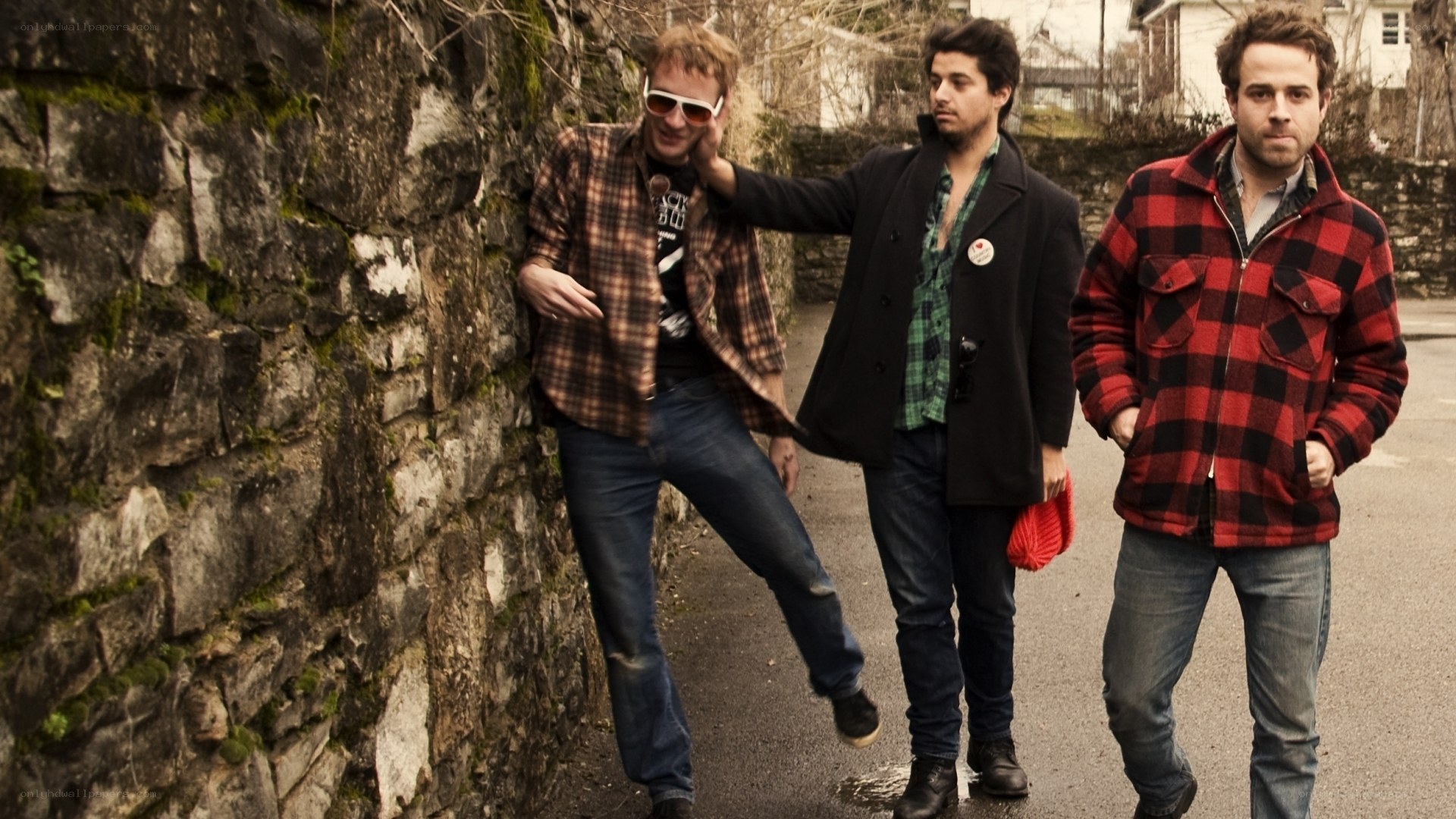 three men posing by a stone wall