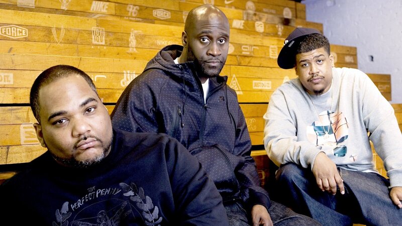 three men posing in front of wooden wall