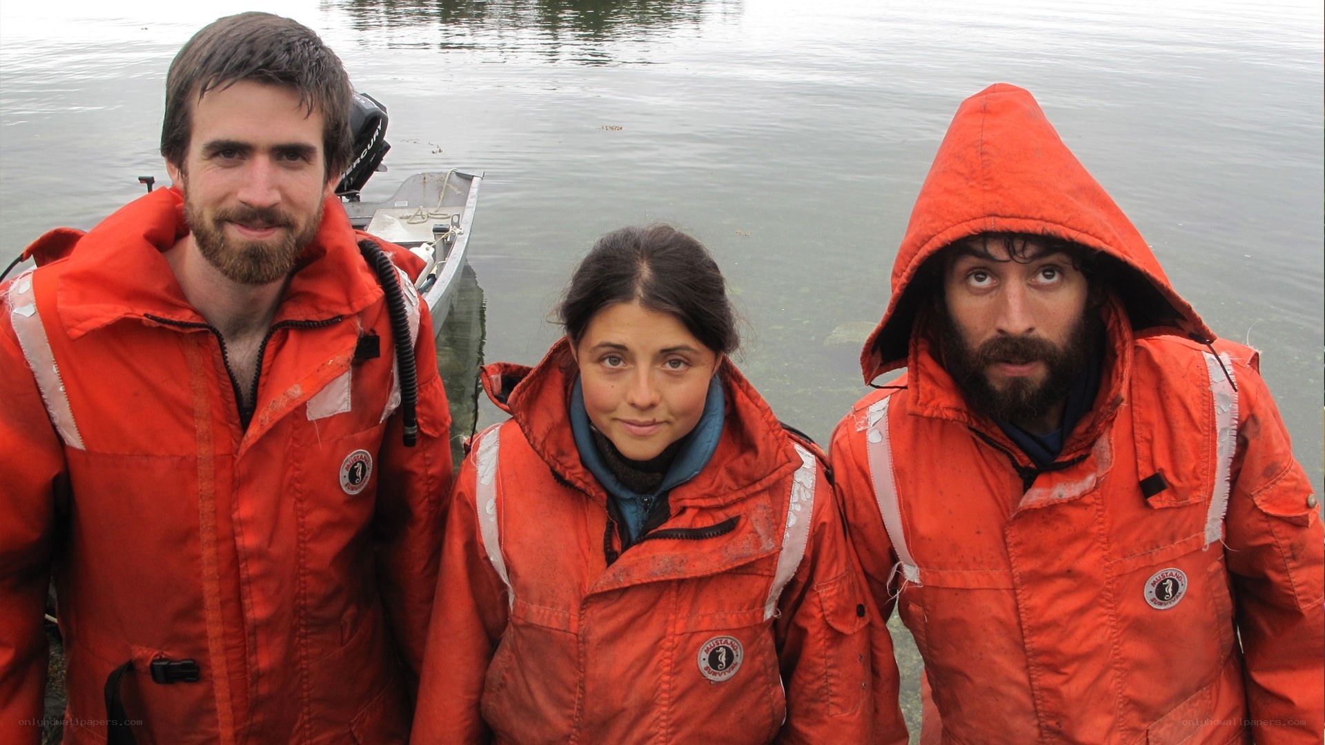 three people in orange jackets by water