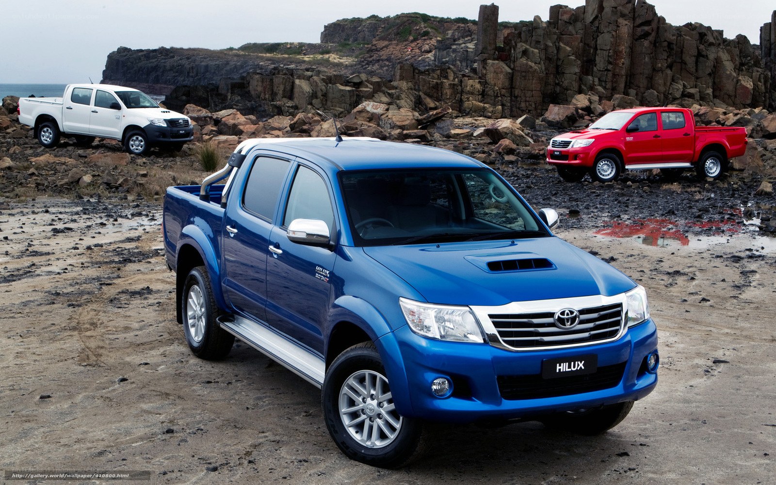 Three Toyota Hilux trucks on a rocky beach