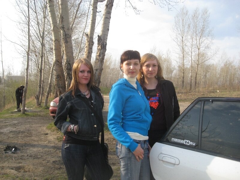 three women posing by a car