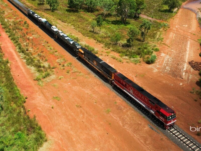 Train carrying cars through red dirt