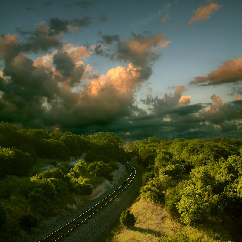 Train track through forest at sunset