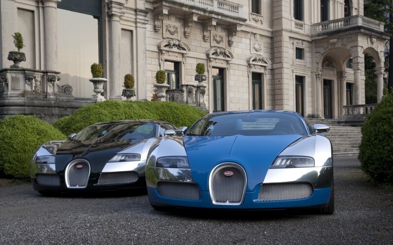 Two Bugatti Veyrons in front of a mansion