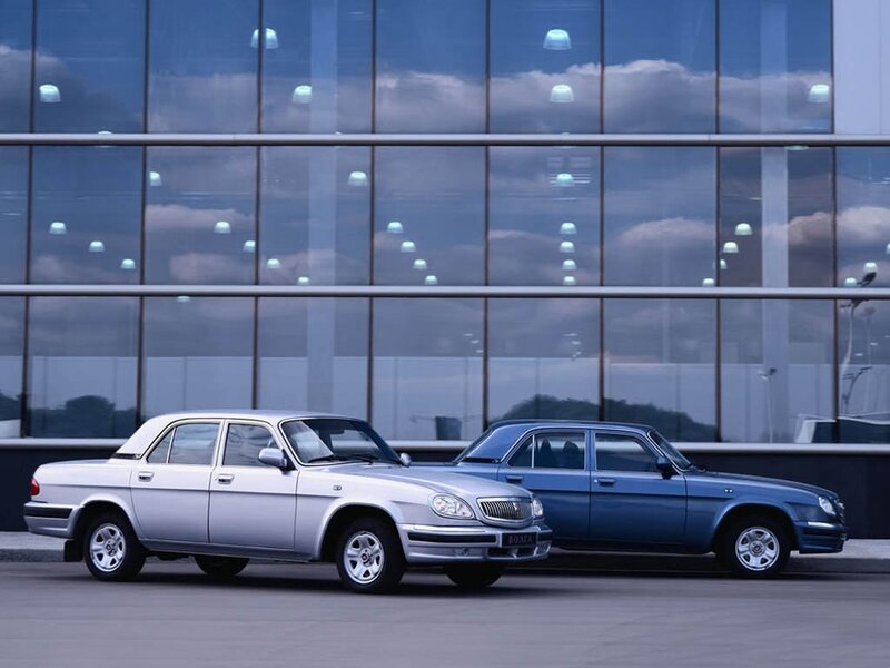 Two classic cars in front of a glass building