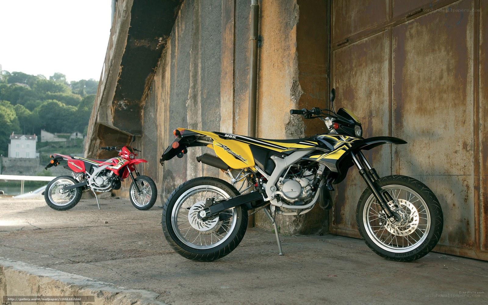 Two dirt bikes parked under a bridge