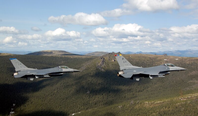 Two fighter jets flying over mountains