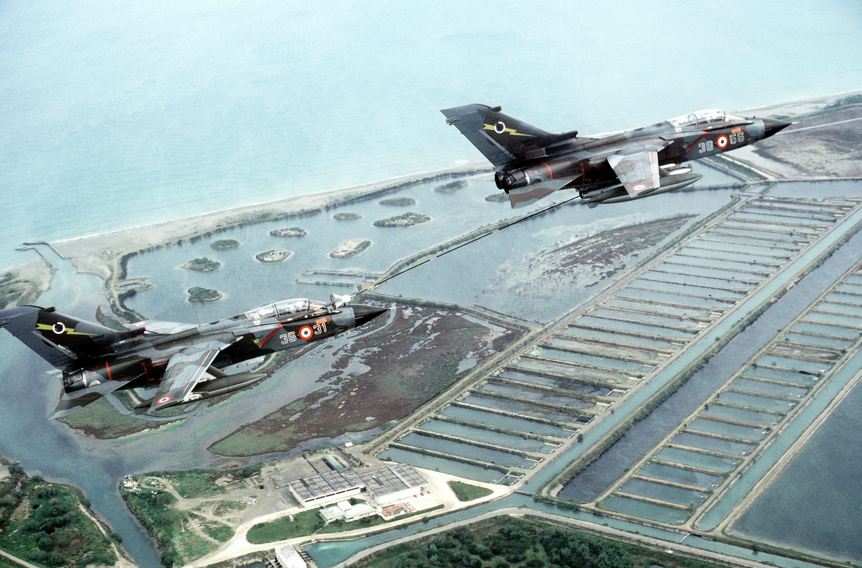 Two fighter jets refueling over coastal area
