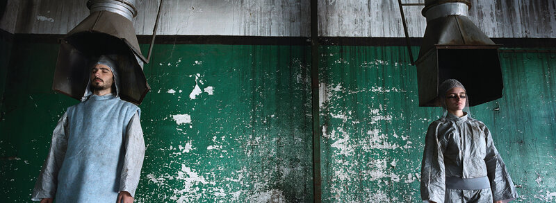 Two figures under hoods in a warehouse