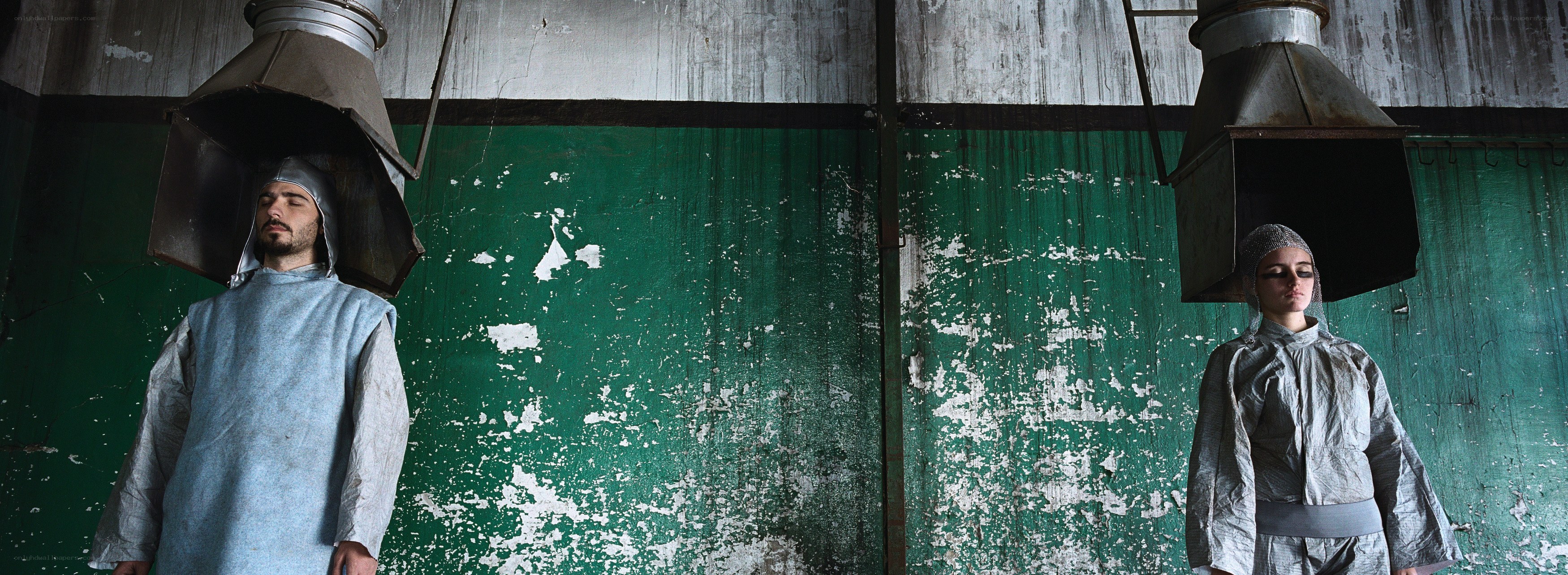Two figures under hoods in a warehouse
