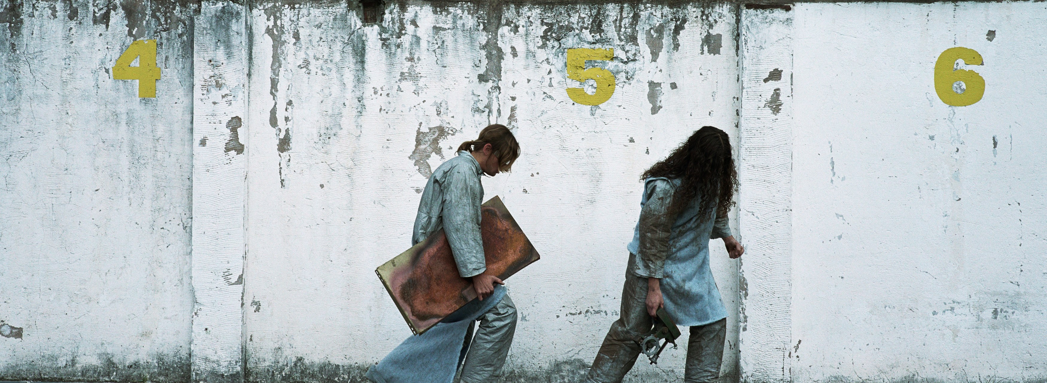 Two figures walk past numbered wall