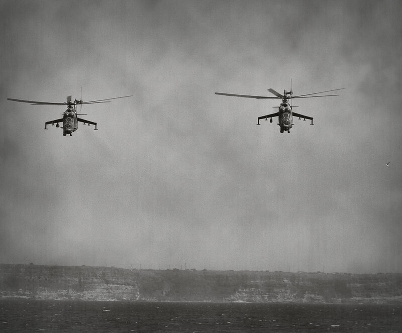 Two helicopters flying over water
