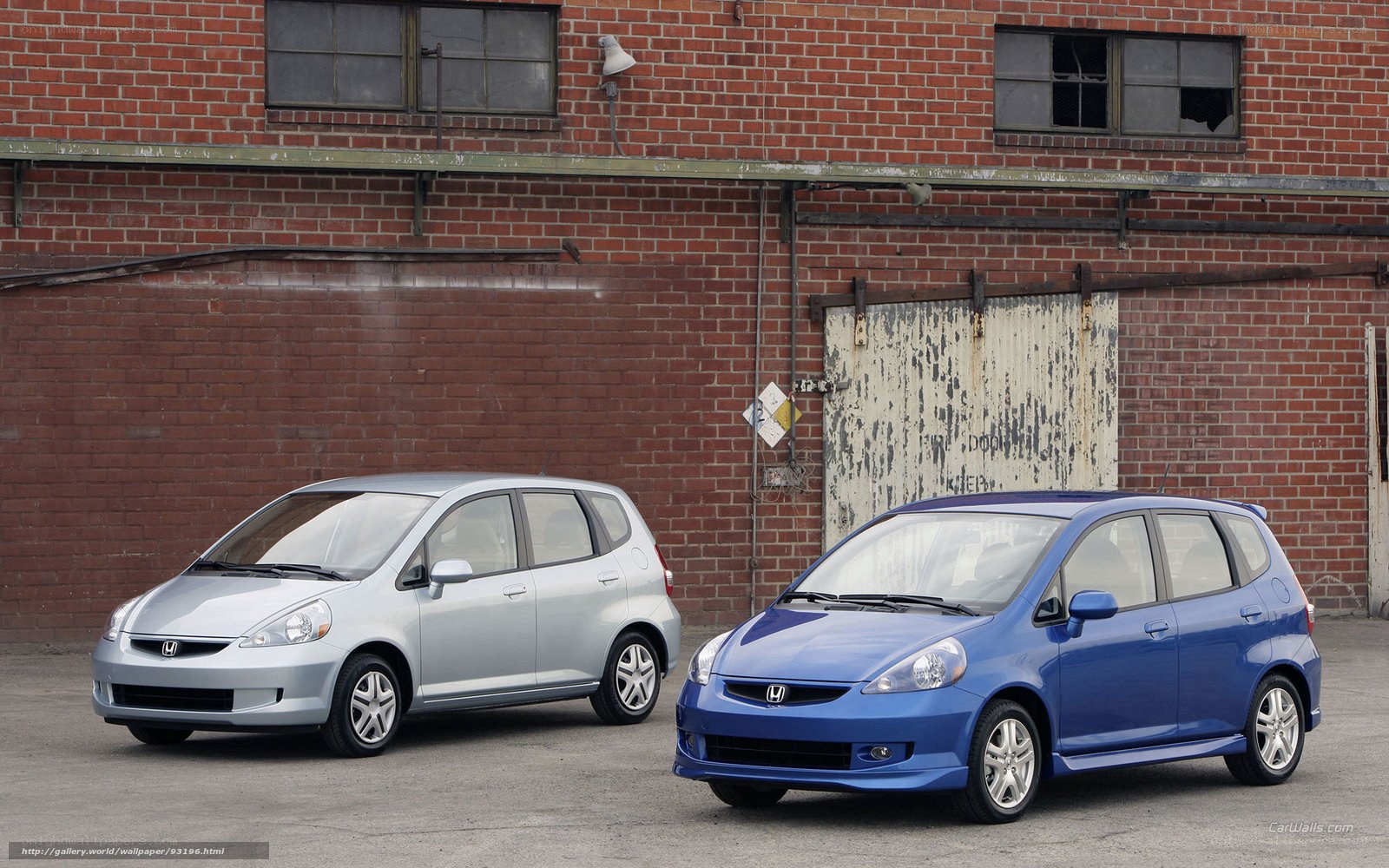 Two Honda Fit cars in front of brick building
