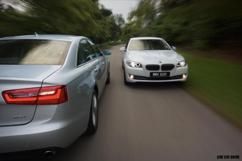 Two luxury sedans driving on a road