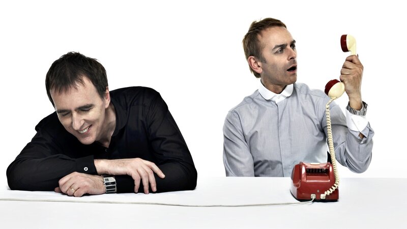 Two men at a table with a red phone