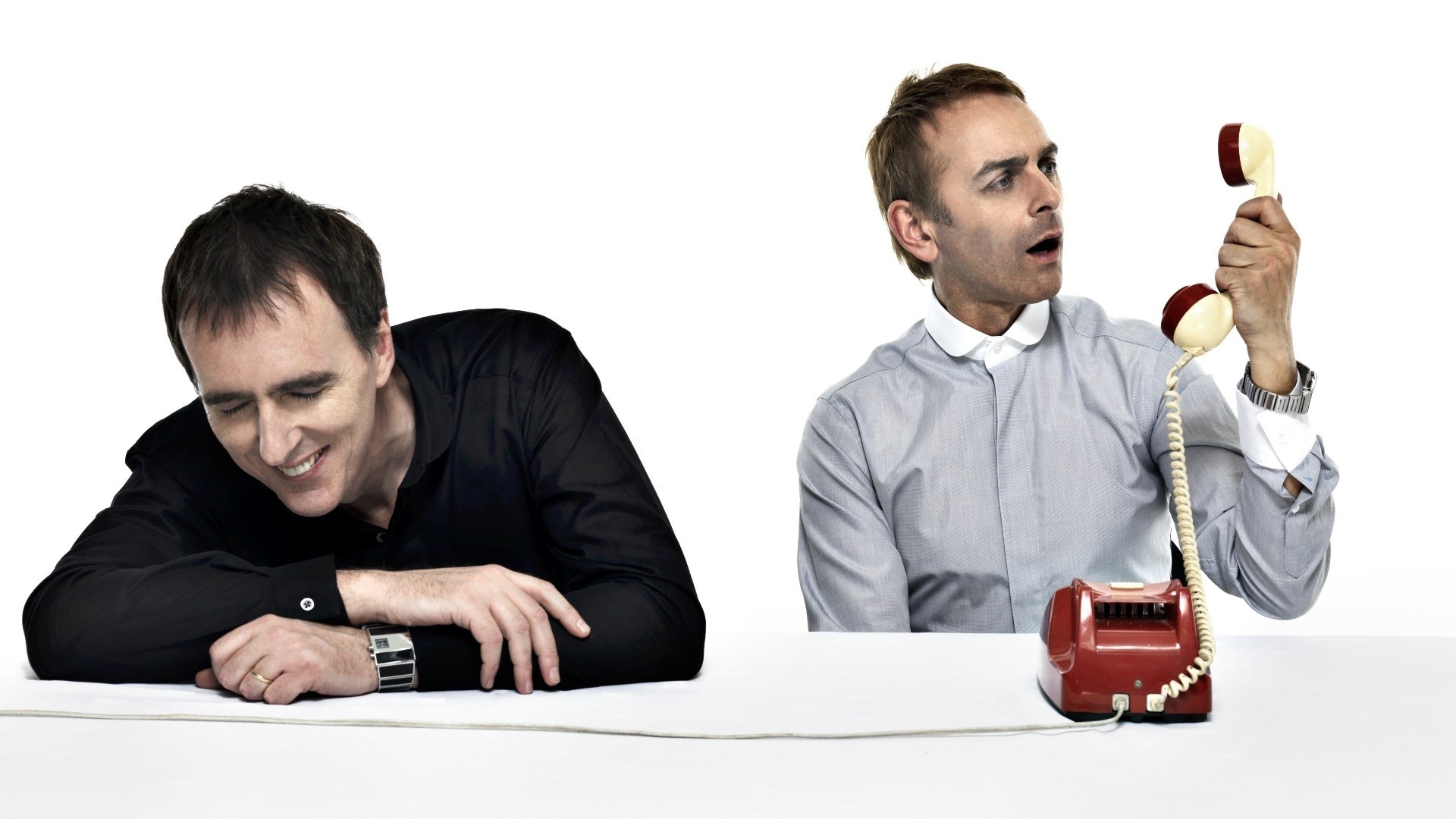 Two men at a table with a red phone