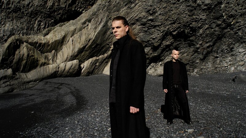 two men in black coats on a rocky beach