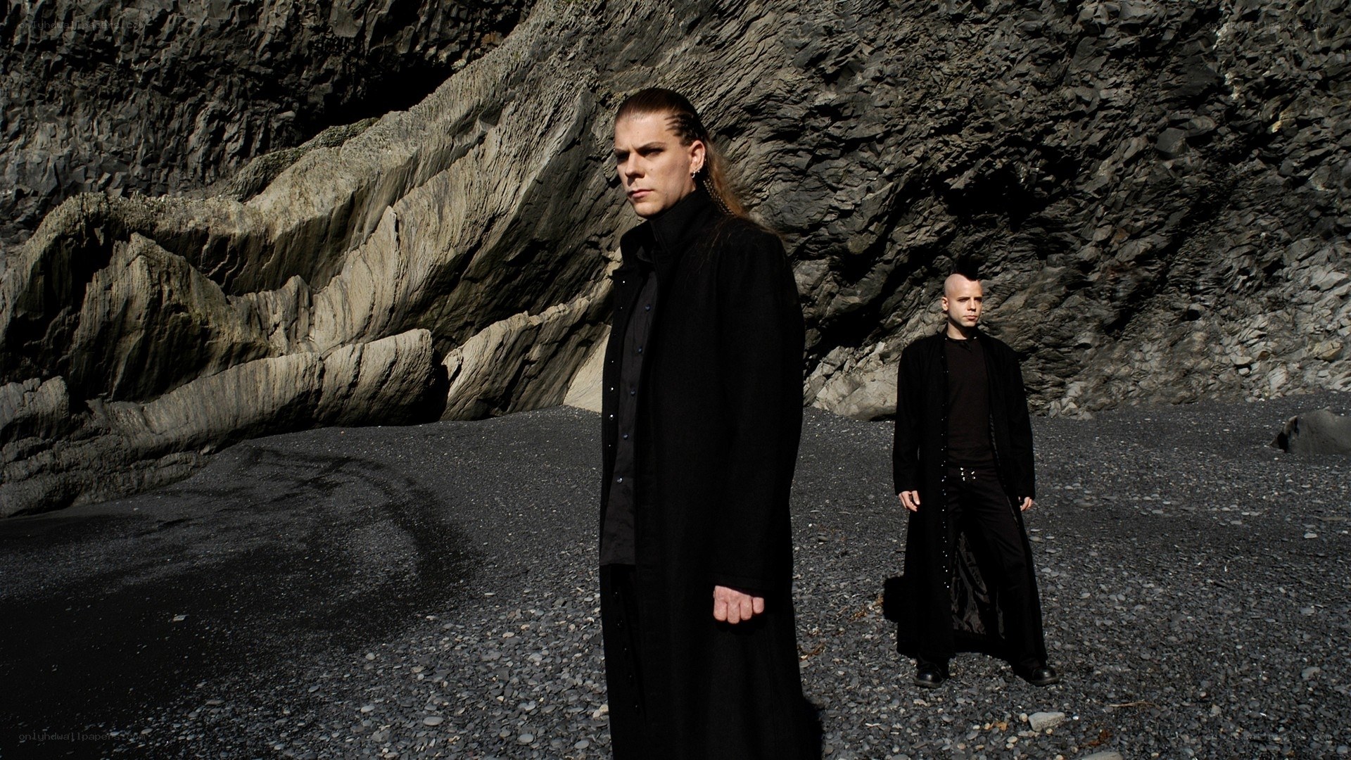 two men in black coats on a rocky beach