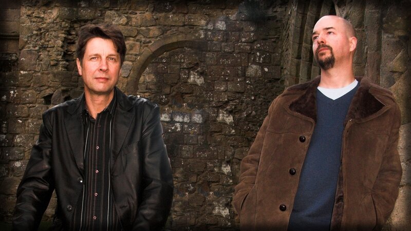two men in front of stone wall