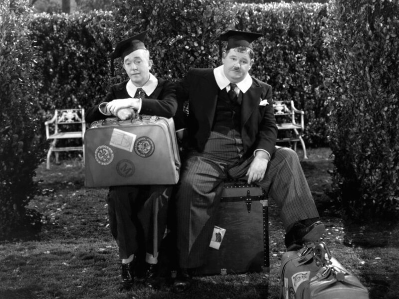 Two men in graduation caps with luggage