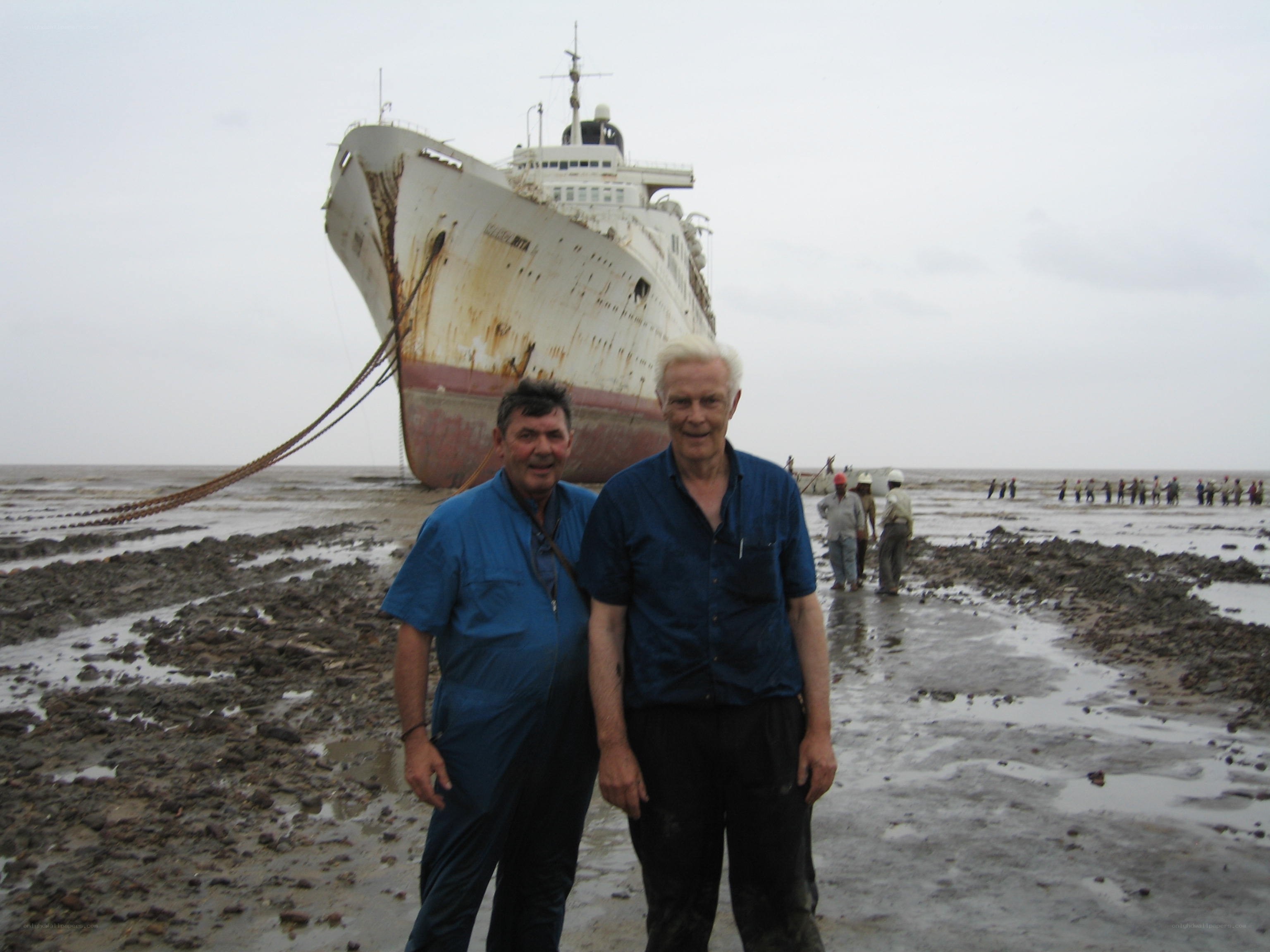 Two men on a beach with a shipwreck