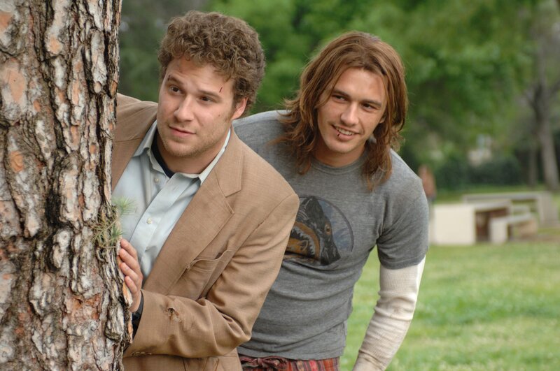 Two men peeking from behind a tree
