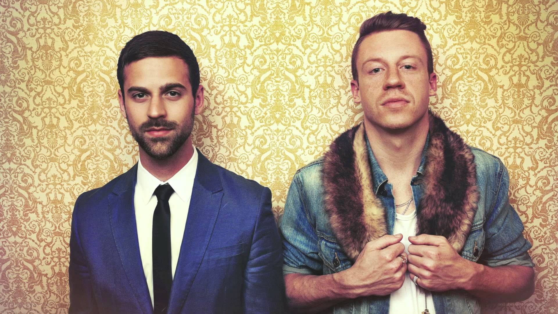 two men posing in front of patterned wallpaper