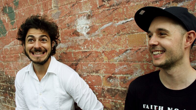 two men smiling by brick wall