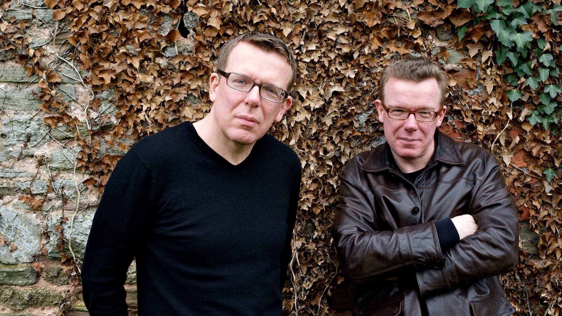 Two men standing by a leafy wall