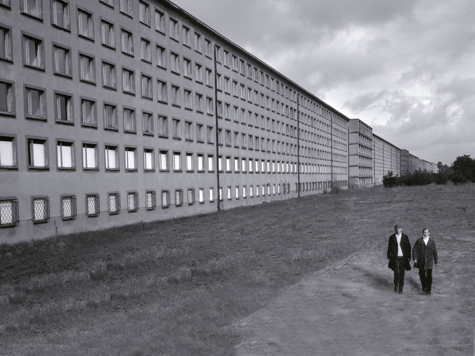 Two men walking near a long building