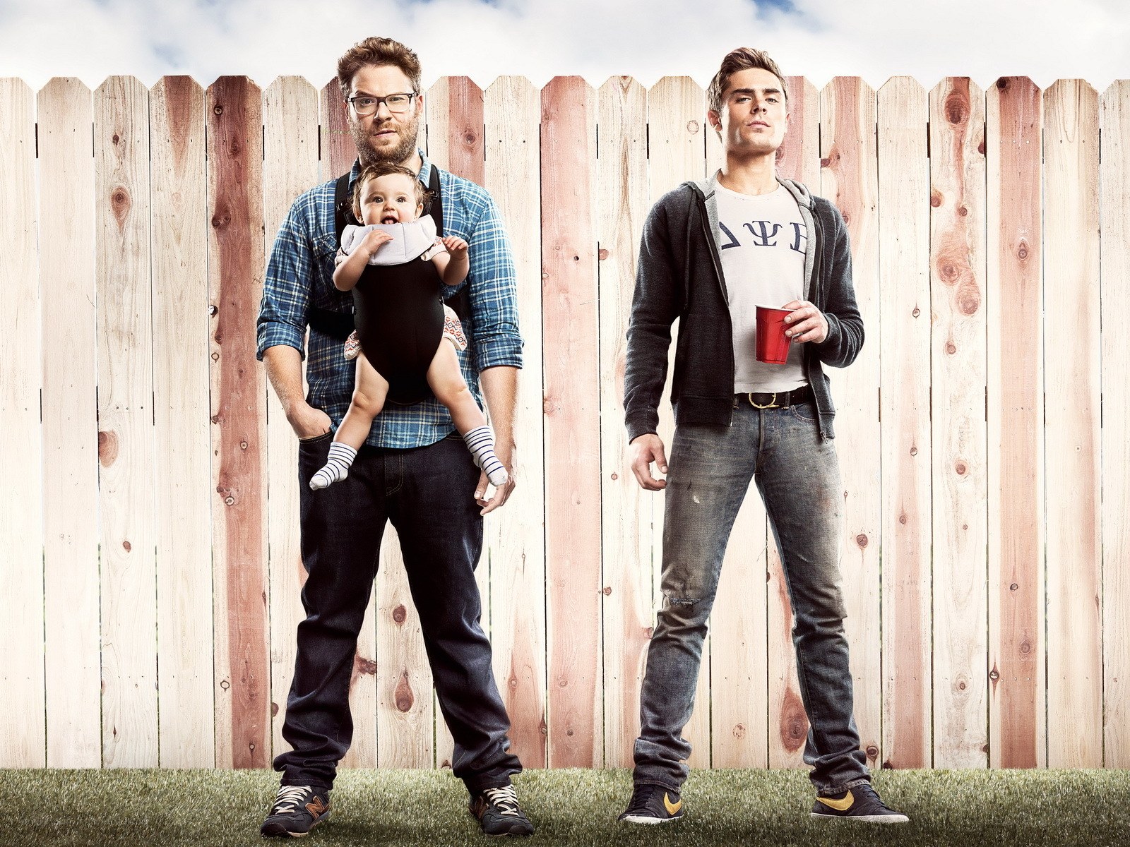 Two men with baby in front of fence