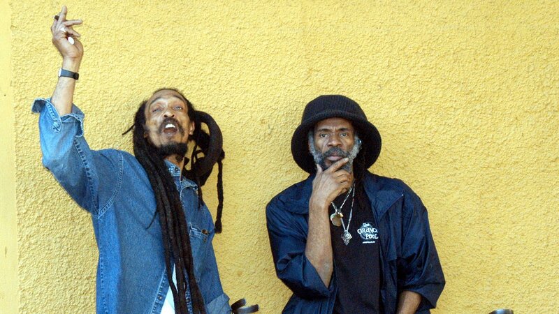 Two men with dreadlocks against yellow wall