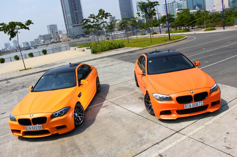 Two orange BMW cars on a city street