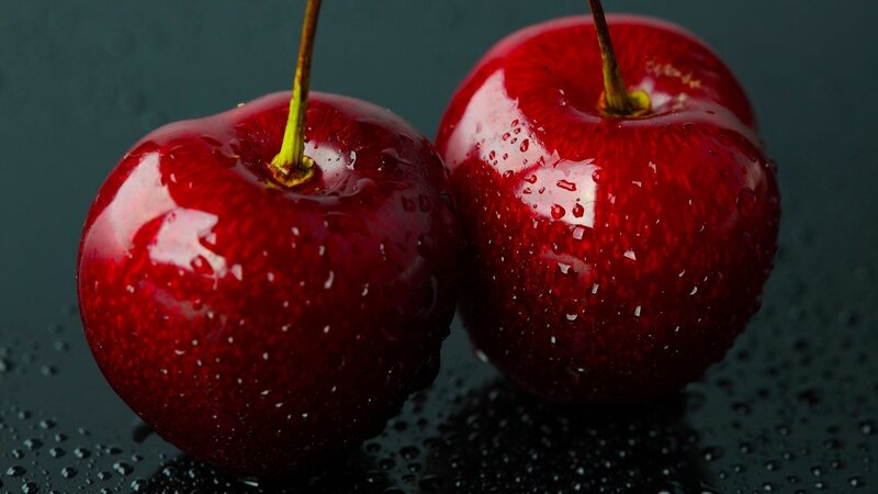 Two wet cherries on dark surface