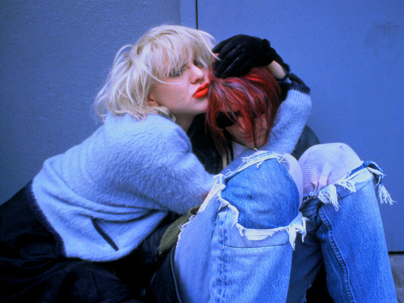 Two women embracing on a blue wall