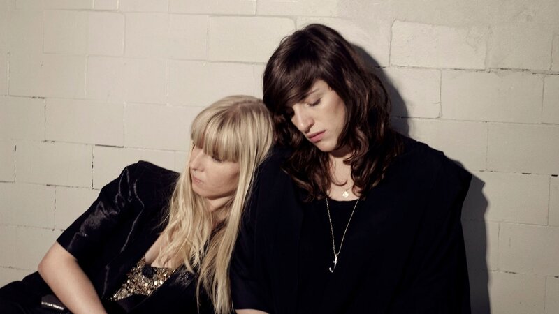 two women leaning against a wall