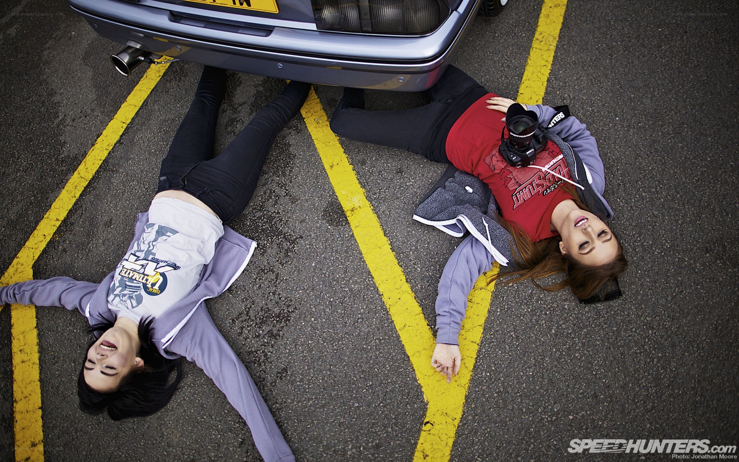 Two women lying under a car