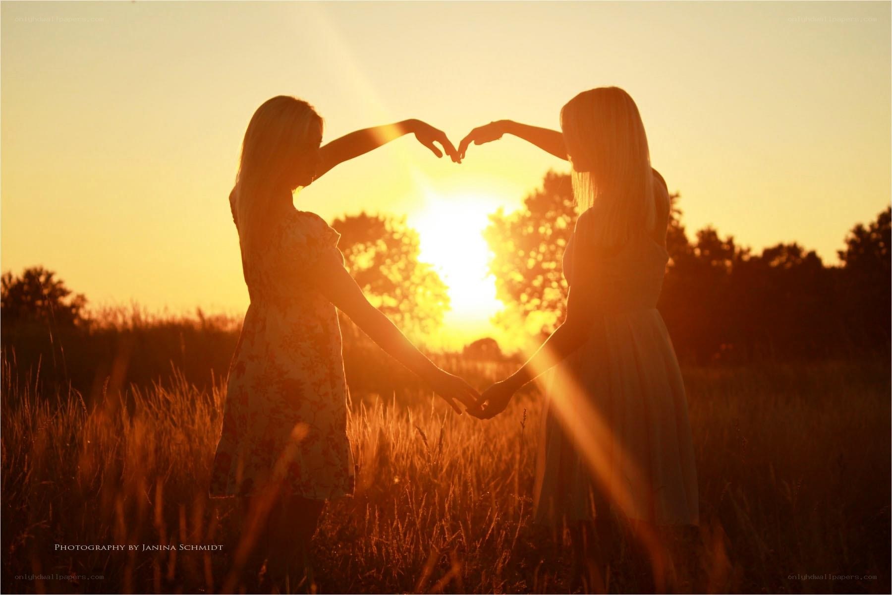 Two women making heart shape at sunset