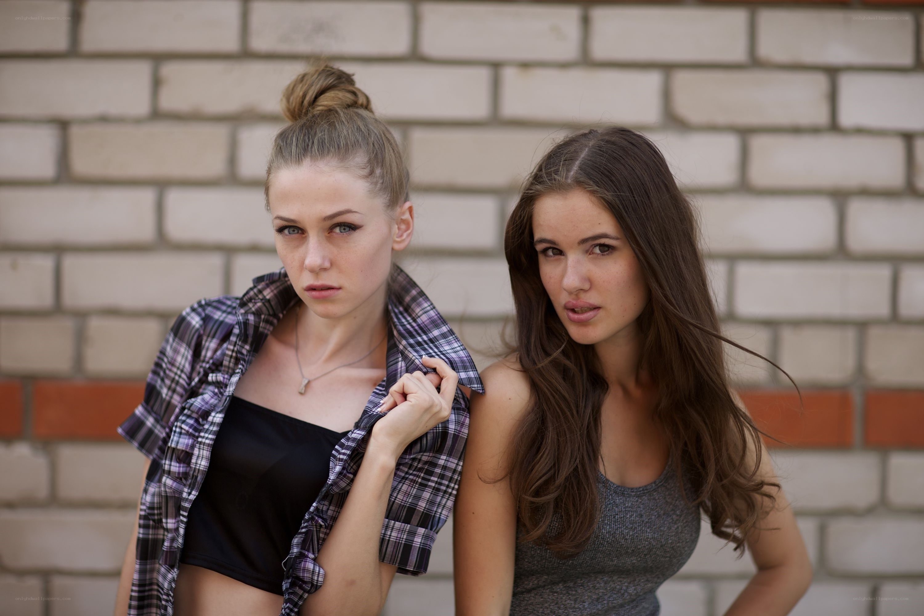 Two women posing against a brick wall