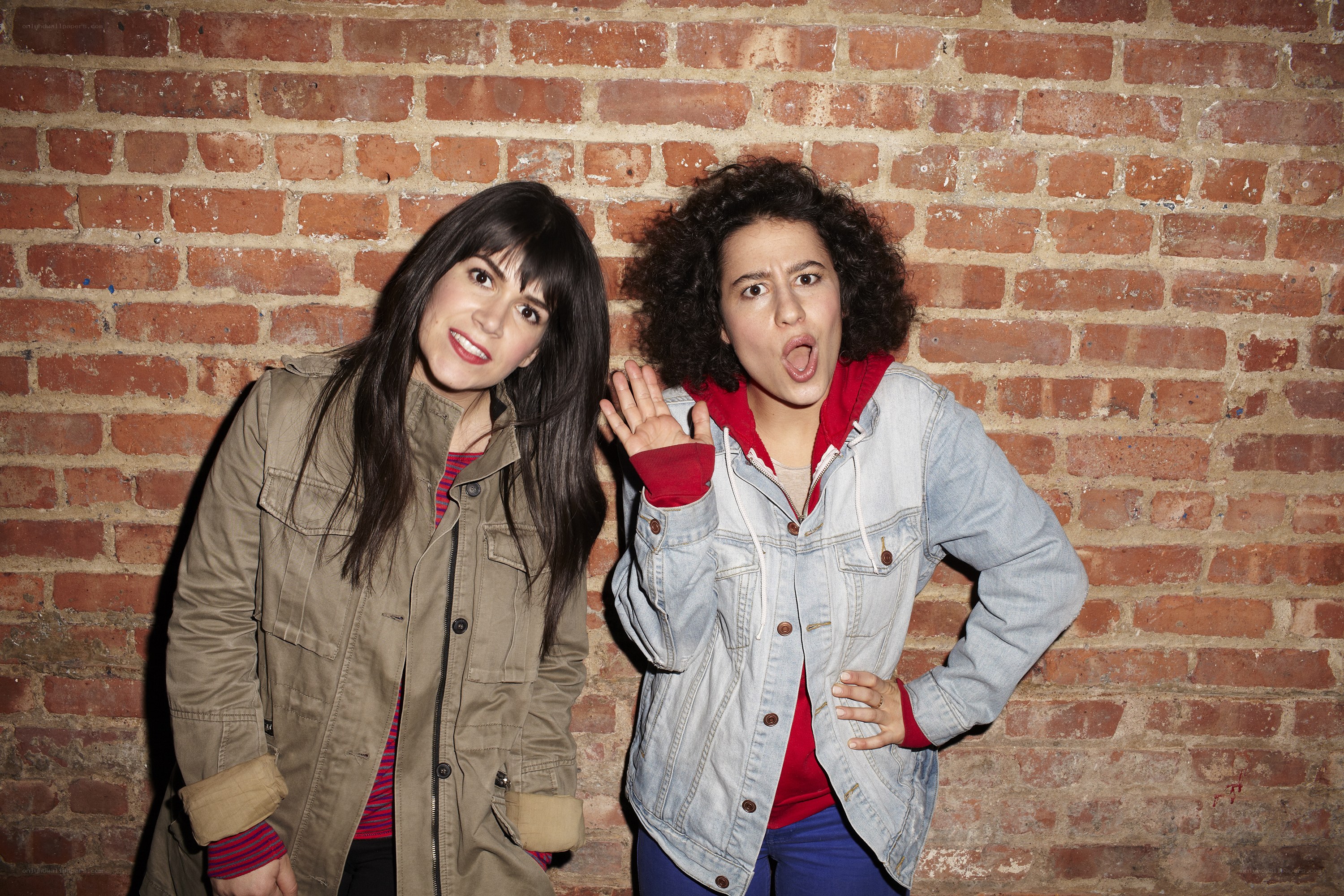 Two women posing against a brick wall